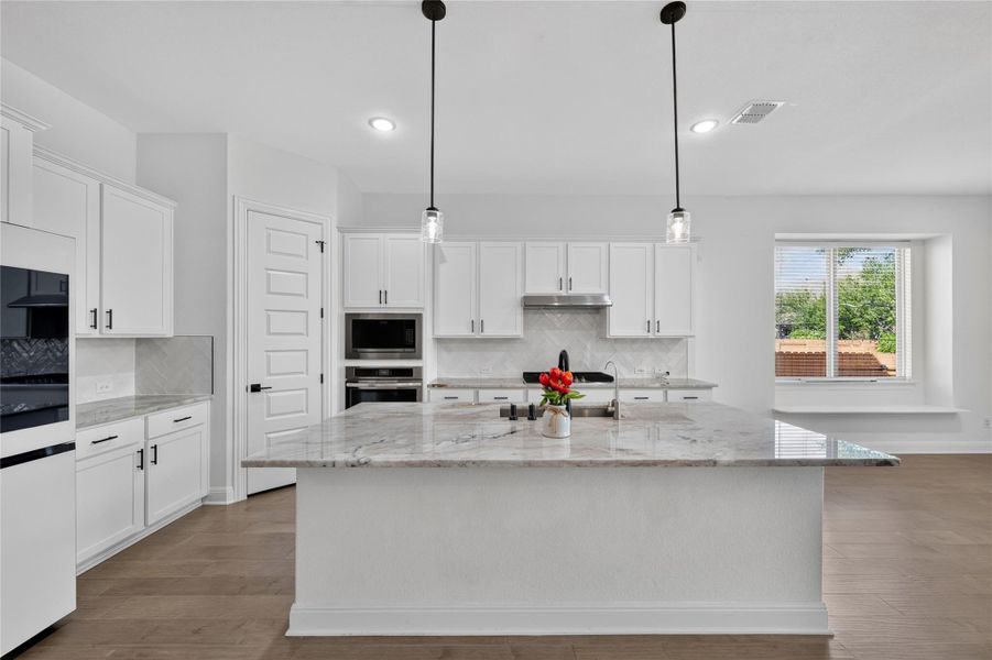 An expansive kitchen island features rich stone countertops and custom cabinetry under recessed lighting. An expansive kitchen island features rich stone countertops and custom cabinetry under recessed lighting.