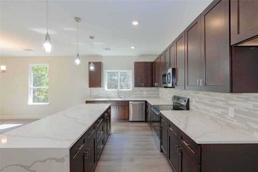 Kitchen featuring pendant lighting, light hardwood / wood-style floors, appliances with stainless steel finishes, and a healthy amount of sunlight