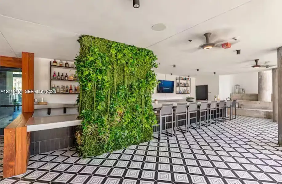 Covered outdoor bar area featuring a geometric-pattern tile floor, a vertical greenery wall, built-in counter seating, and wood-accented structural pillars Covered outdoor bar area featuring a geometric-pattern tile floor, a vertical greenery wall, built-in counter seating, and wood-accented structural pillars