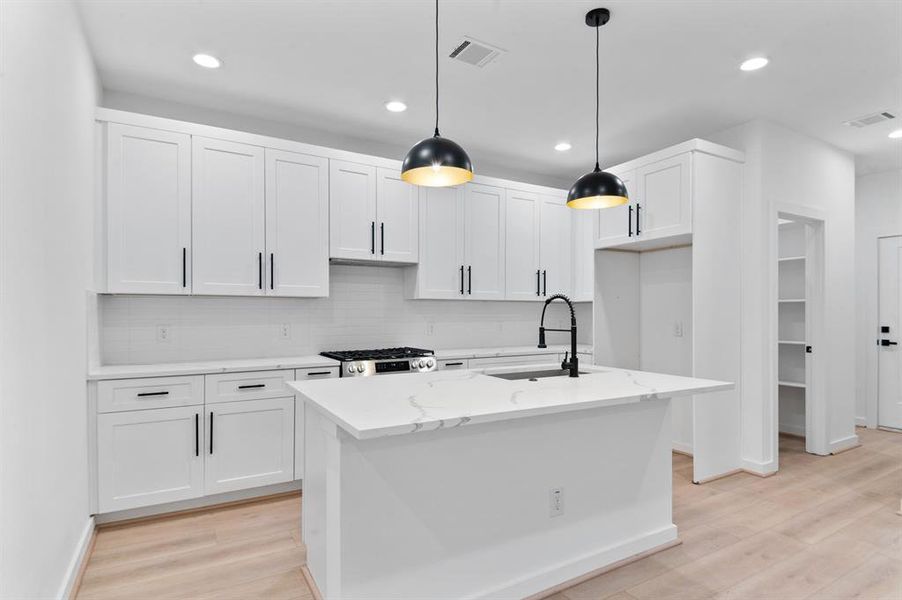 This modern kitchen features sleek white cabinetry with black handles, a central island with a marble countertop and sink, and contemporary pendant lighting. The space is bright and open, offering ample storage and a stylish, clean design.