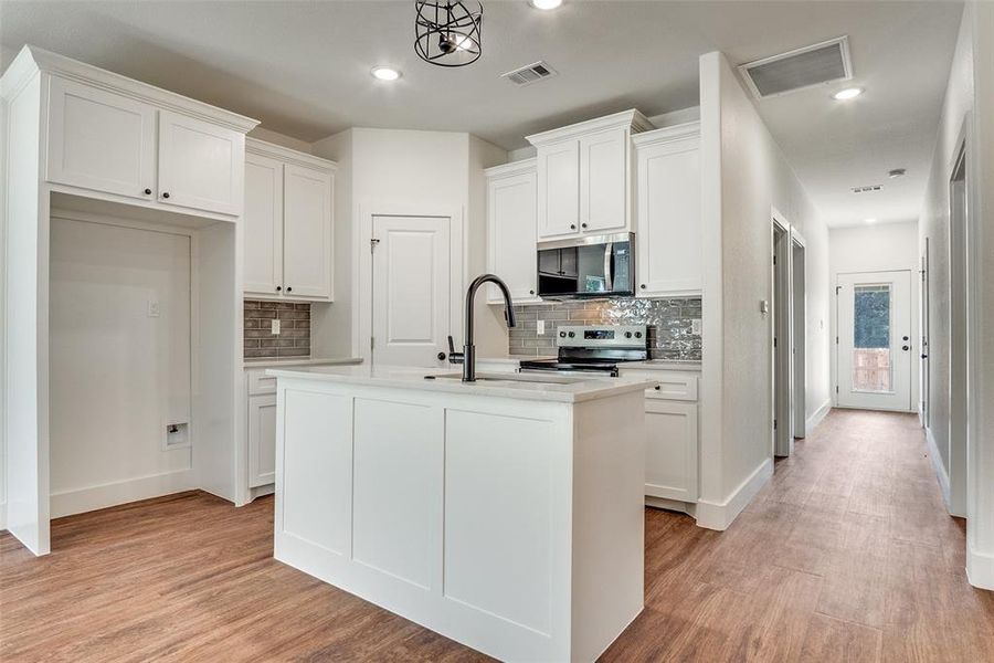 Kitchen with white cabinets, backsplash, light wood finished floors, stainless steel appliances, and recessed lighting