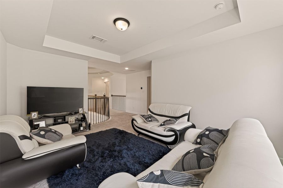 This gameroom features modern seating, a large TV, and plush carpeting. It's bright and airy with neutral walls, offering a comfortable area for relaxation.