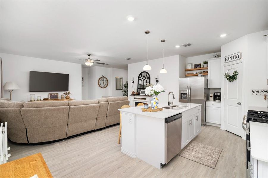 This property features an open-concept living area with light-colored flooring, a kitchen island with a sink and stainless steel dishwasher, and a pantry with a door