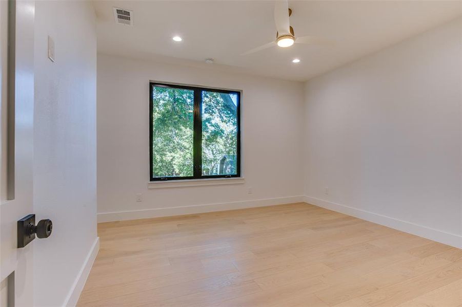 Secondary bedroom with warm wood floors, ceiling fan, and large windows overlooking the treed setting.