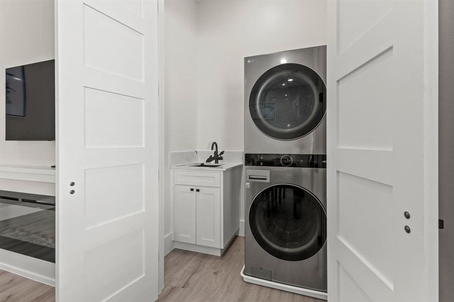 Laundry area featuring stacked washer / dryer, light wood finished floors, and cabinet space