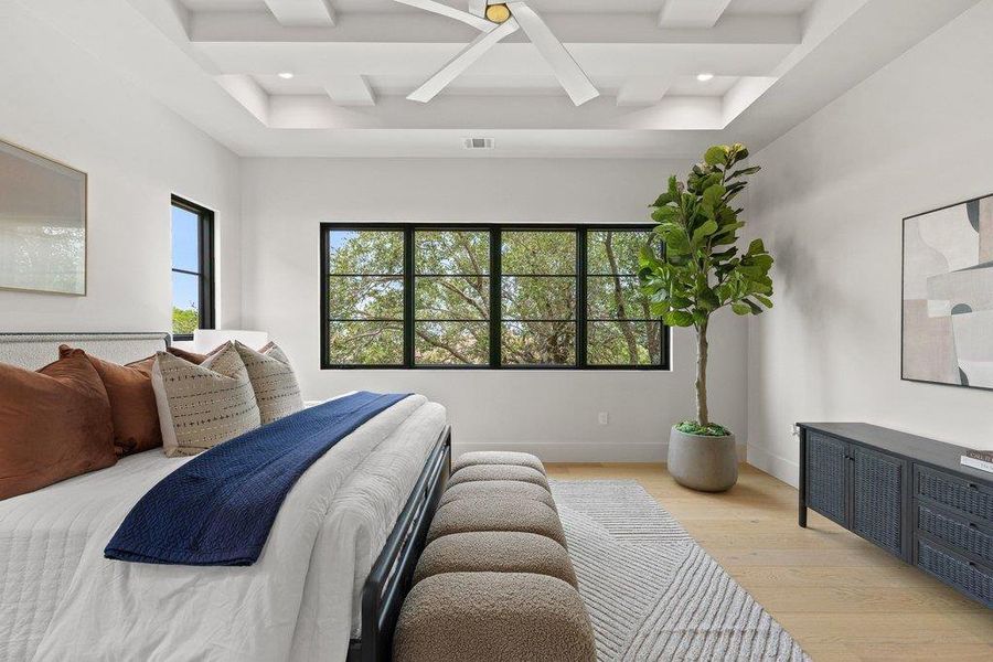 Spacious room featuring a tiered coffered ceiling with a modern ceiling fan, light wood-finish flooring, and multiple black-framed windows