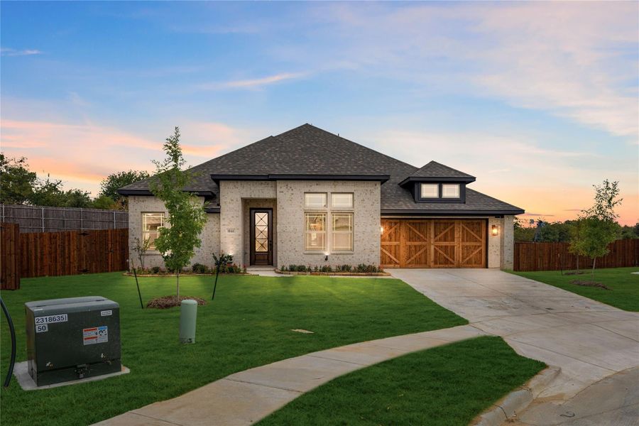 Single-story home with light brick exterior, wood two-car garage doors, and manicured front lawn at dusk Single-story home with light brick exterior, wood two-car garage doors, and manicured front lawn at dusk