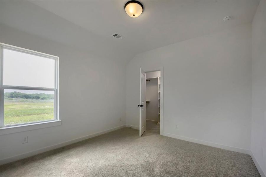 Bright interior space featuring a large window, neutral wall paint, carpet flooring, a ceiling-mounted light fixture, and an open doorway revealing built-in shelving Bright interior space featuring a large window, neutral wall paint, carpet flooring, a ceiling-mounted light fixture, and an open doorway revealing built-in shelving