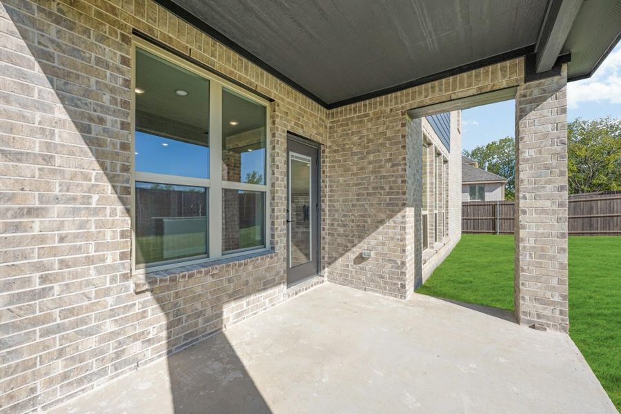 Covered back patio with concrete floor, brick exterior, glass door, and fenced backyard with green lawn.