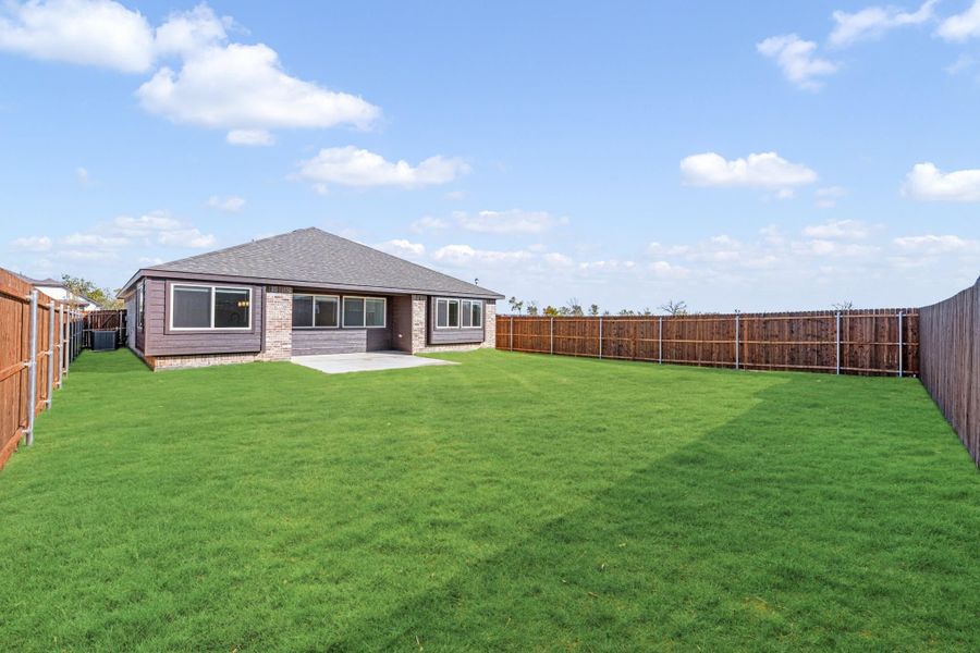 Backyard with large green lawn, wood privacy fence, and single-story brick home with patio