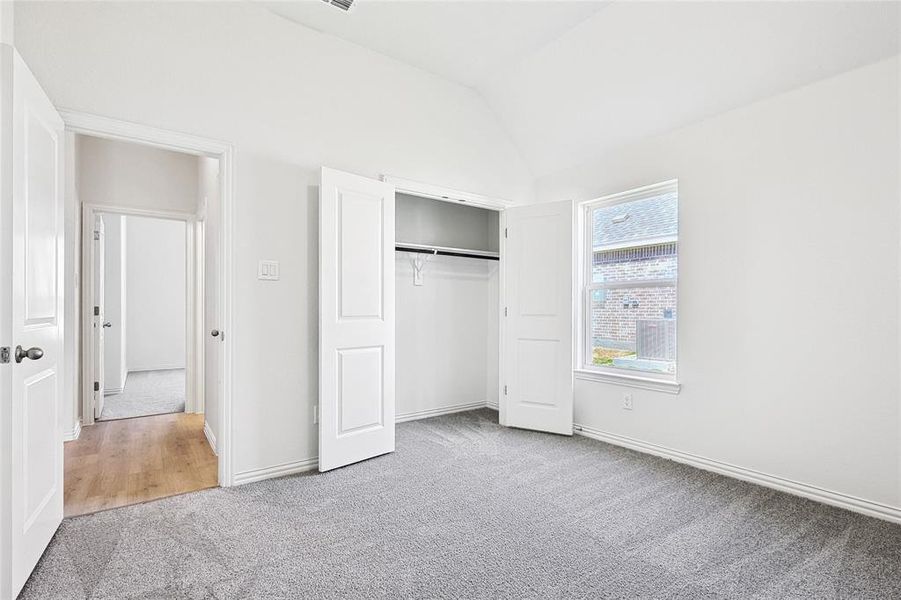 Unfurnished bedroom featuring lofted ceiling, a closet, and light colored carpet