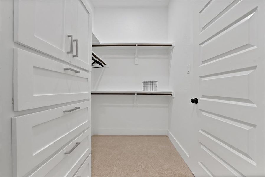 Walk-in closet with built-in white shaker cabinetry, brushed nickel hardware, and light-tone carpeting