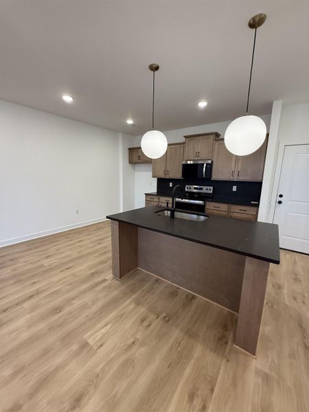 Kitchen featuring dark countertops, hanging light fixtures, and a kitchen island with sink