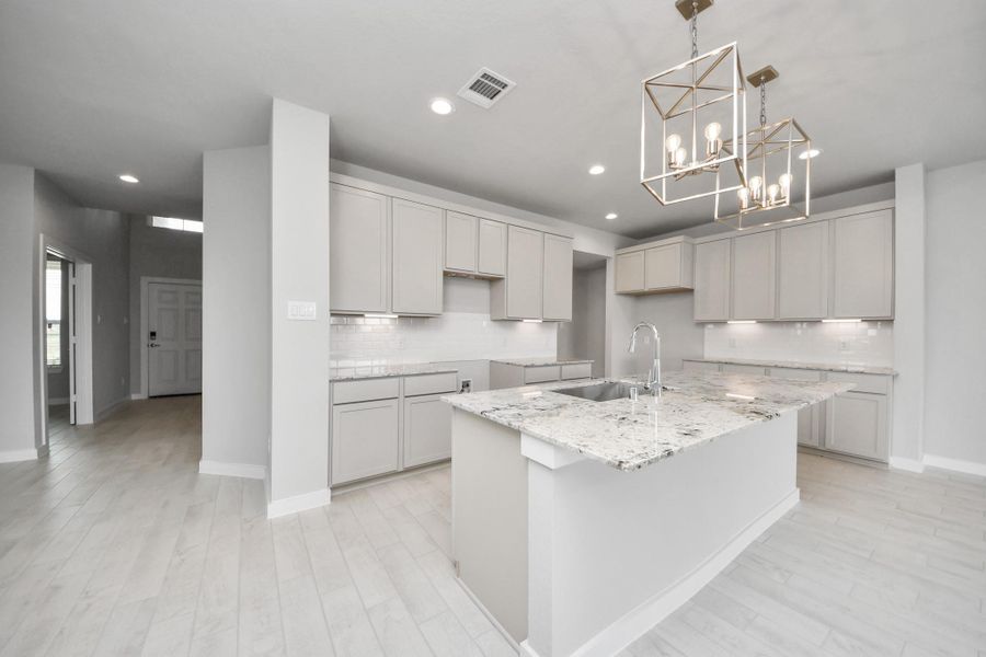 This kitchen is truly a chef's dream! This haven Boasts high ceilings, recessed & pendant lighting, stained wood cabinets, granite countertops, stainless steel appliances, a modern tile backsplash.  All of this overlooks your expansive family room, creating a perfect space for culinary delights and family gatherings. Sample photo of completed home with similar floor plan. Actual colors and selections may vary.