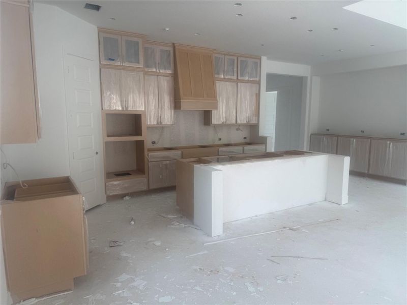 Kitchen featuring light brown cabinetry, custom range hood, a center island, and glass insert cabinets