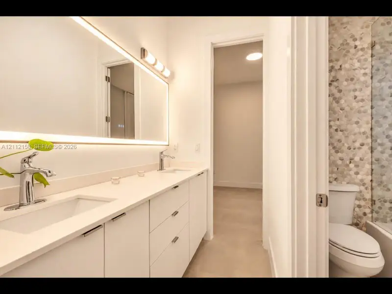 Modern bathroom with a dual-sink vanity, oversized LED-lit mirror, and stylish tile shower accents