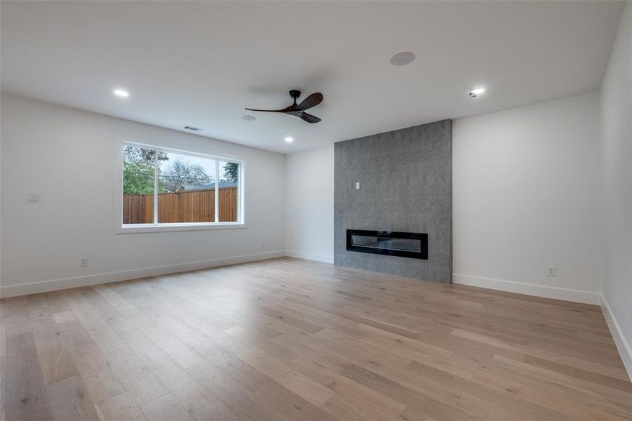 Living room with light wood-style flooring, ceiling fan, a fireplace, and recessed lighting