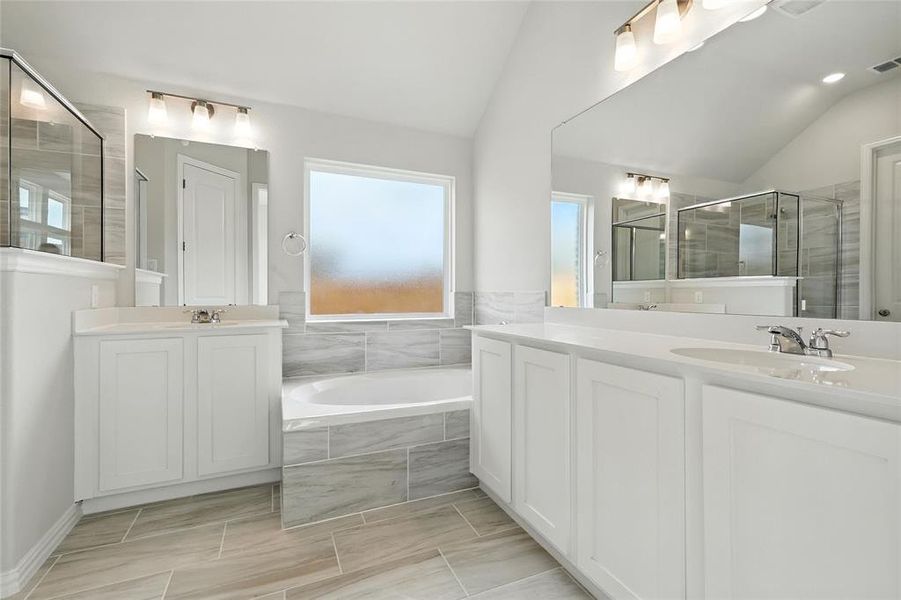 Full bath featuring vaulted ceiling, a garden tub, two vanities, and a shower stall