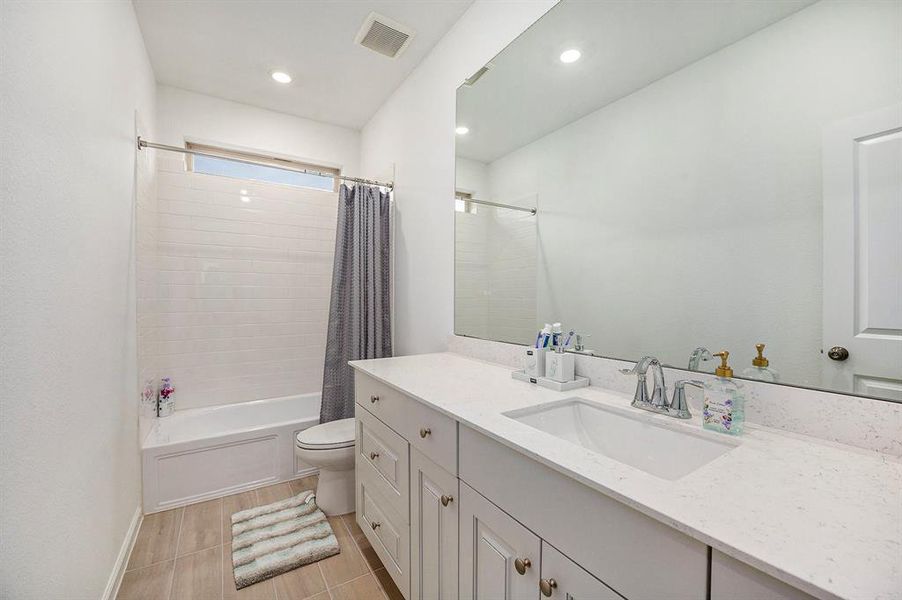 This bathroom features a clean, modern design with a white vanity and ample storage. It includes a spacious mirror, a tub-shower combo with a curtain, and neutral tile flooring. The space is well-lit, creating a bright and inviting atmosphere.