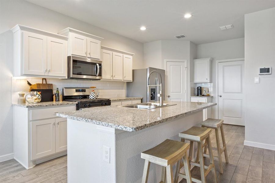 Kitchen with stainless steel appliances, light wood-style floors, an island with sink, decorative backsplash, and white cabinetry Kitchen with stainless steel appliances, light wood-style floors, an island with sink, decorative backsplash, and white cabinetry