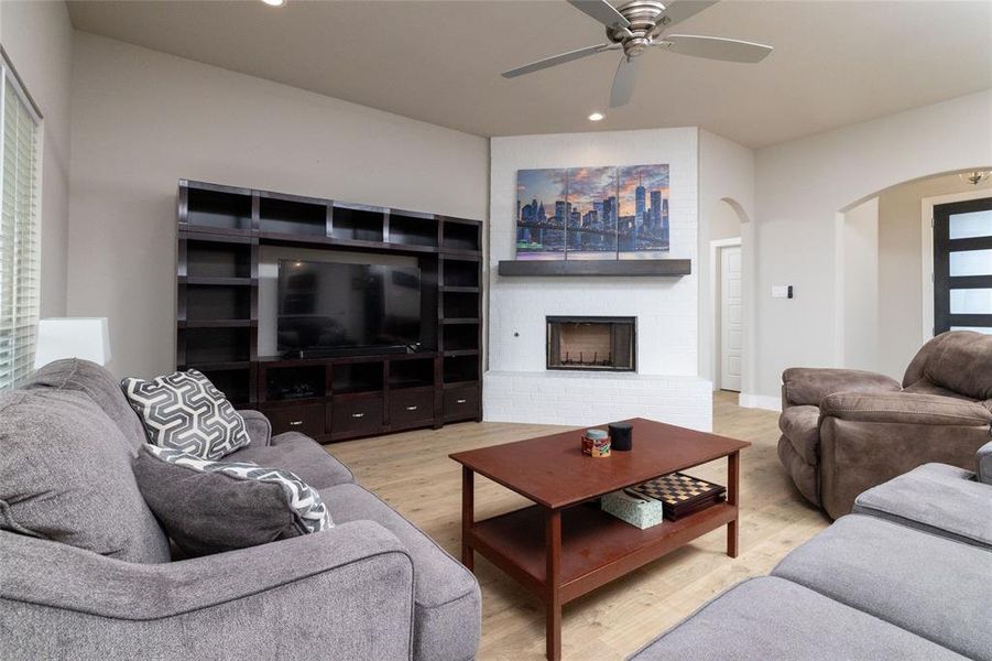 Living area with light wood-type flooring, a brick fireplace, recessed lighting, ceiling fan, and arched walkways