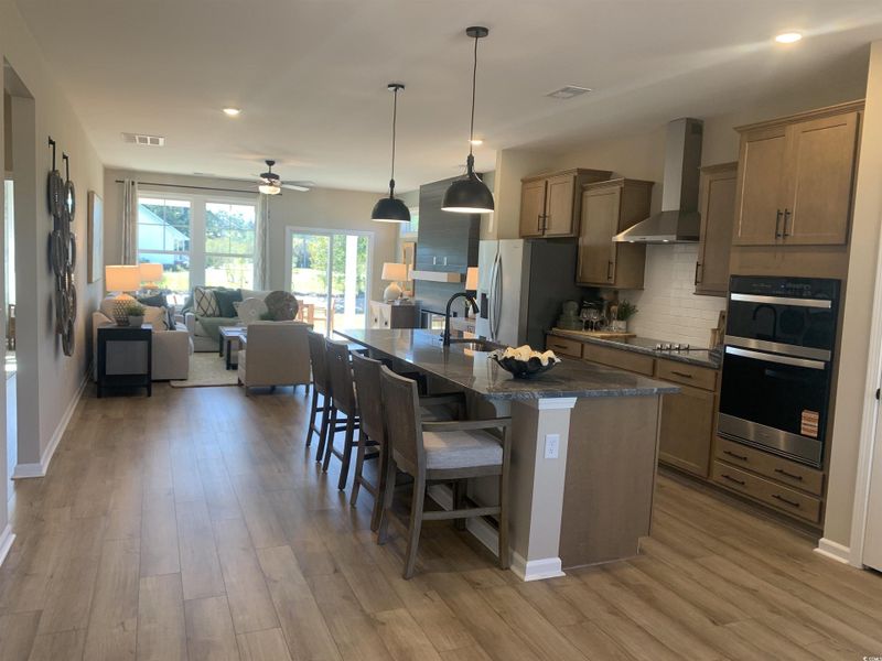 Kitchen with pendant lighting, wall chimney range hood, open floor plan, decorative backsplash, and a breakfast bar