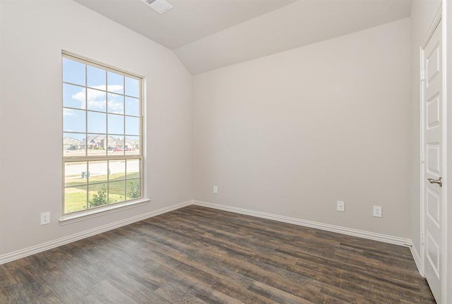 Empty room featuring dark hardwood / wood-style floors, vaulted ceiling, and a healthy amount of sunlight