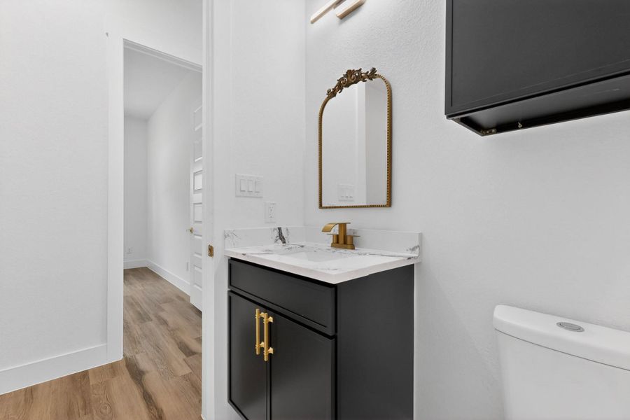 A well-appointed powder room features a chic vanity with a marble-patterned countertop and elegant gold hardware.