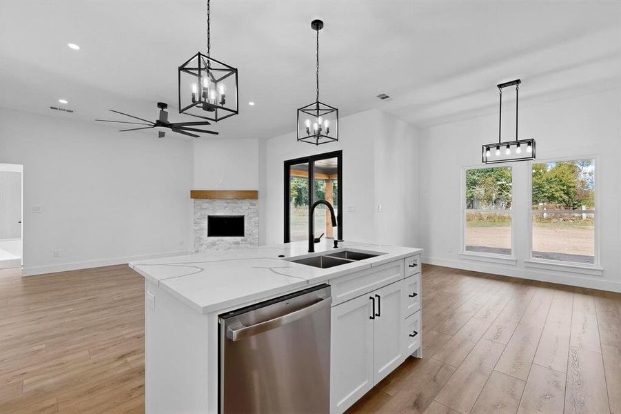 Kitchen featuring stainless steel dishwasher, light wood-style flooring, decorative light fixtures, a center island with sink, and white cabinets