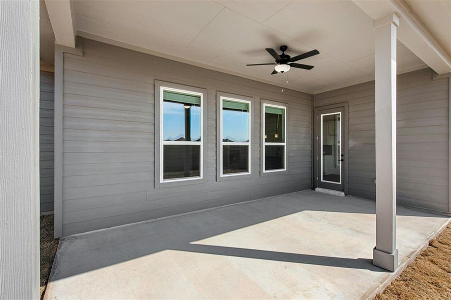 Covered patio featuring a ceiling fan, three windows with white trim, a glass-paneled exterior door, and a concrete slab