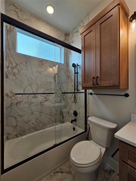 This bathroom features a modern design with marble-patterned tiles, a sleek glass-enclosed bathtub with black fixtures, and a wood cabinet for storage. A frosted window provides natural light while maintaining privacy. This bathroom features a modern design with marble-patterned tiles, a sleek glass-enclosed bathtub with black fixtures, and a wood cabinet for storage. A frosted window provides natural light while maintaining privacy.