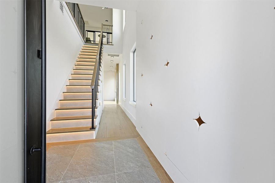 Same floorplan - different finishes. The bright entryway showcases light oak flooring, integrated LED stair lighting, and unique diamond-shaped wall cutouts.