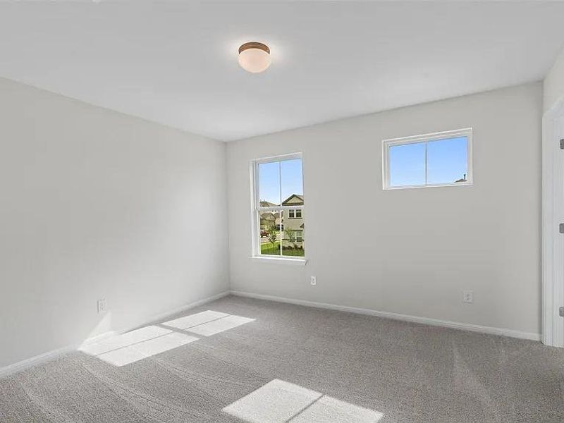 A well-lit bedroom features plush carpeting and multiple windows.