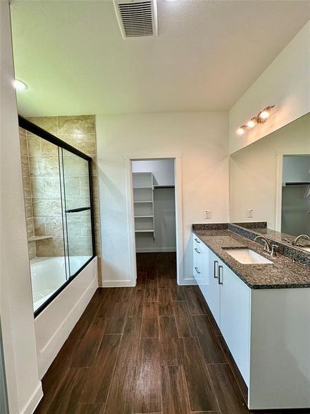 Bathroom featuring a wood-finish tile floor, a shower-tub combination with a tiled surround and glass enclosure, and a double vanity with stone countertops and undermount sinks Bathroom featuring a wood-finish tile floor, a shower-tub combination with a tiled surround and glass enclosure, and a double vanity with stone countertops and undermount sinks