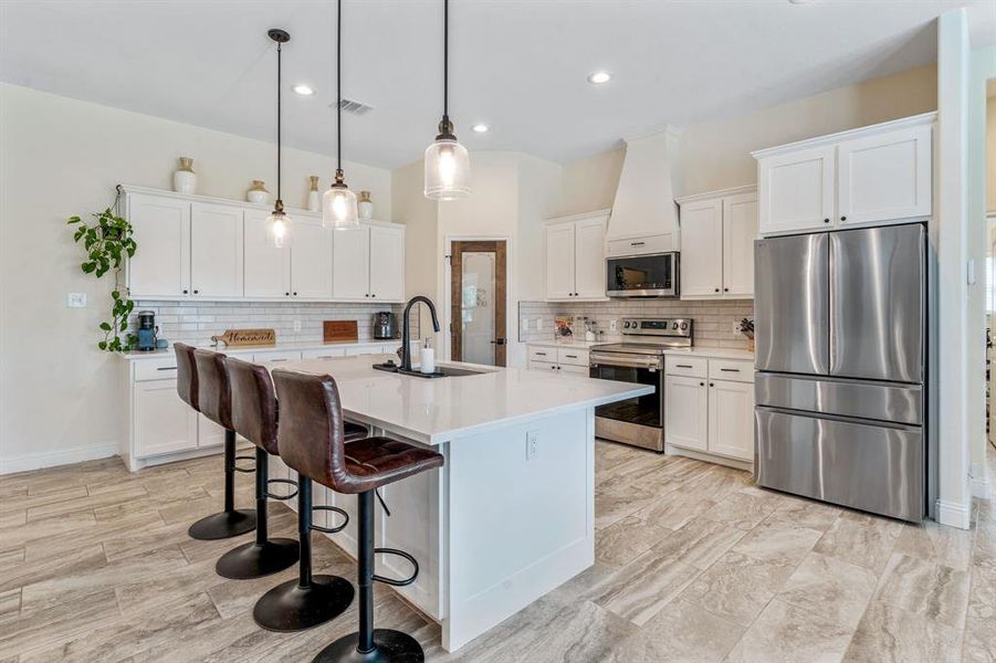 Kitchen featuring appliances with stainless steel finishes, a kitchen bar, pendant lighting, a center island with sink, and white cabinetry Kitchen featuring appliances with stainless steel finishes, a kitchen bar, pendant lighting, a center island with sink, and white cabinetry