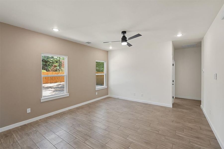 Spacious room featuring wood-look tile flooring, a modern black ceiling fan with integrated lighting, and multiple recessed light fixtures