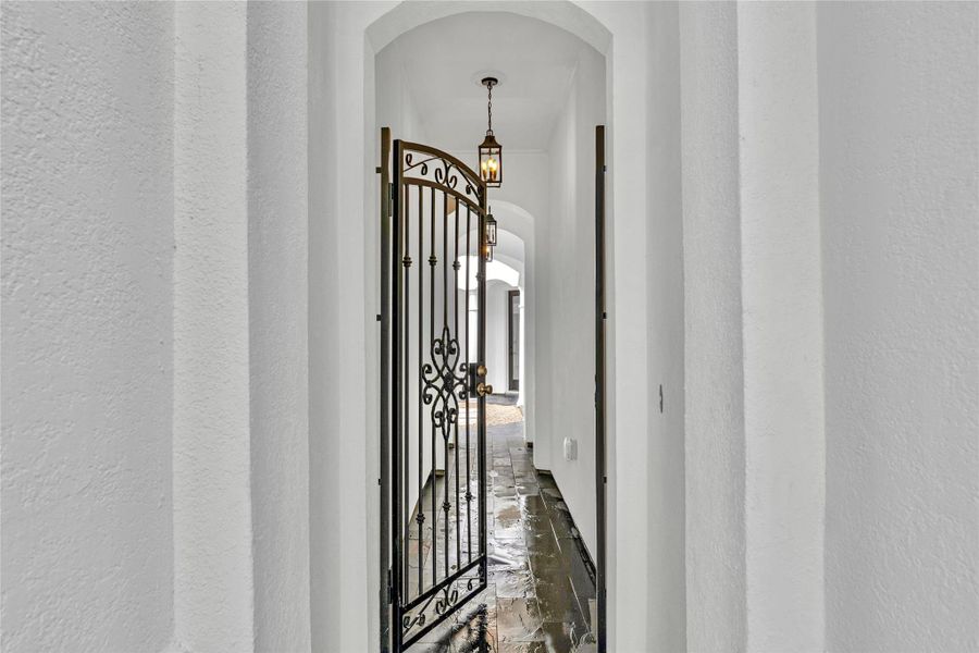 The wrought iron gate opens to an arched corridor softly illuminated by hanging lanterns.