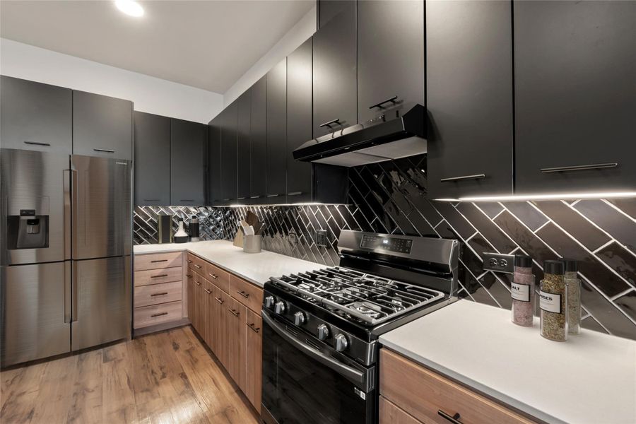 Kitchen with stainless steel fridge, range with gas stovetop, under cabinet range hood, tasteful backsplash, and light countertops
