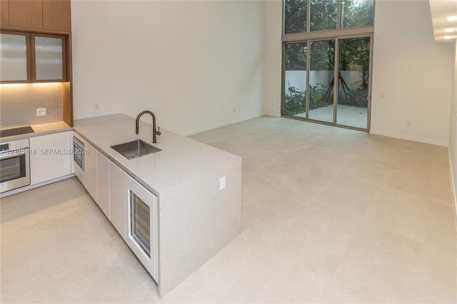Kitchen featuring a stone-surface island, built-in wine refrigeration, high-ceiling glass sliding doors, and large-format tile flooring