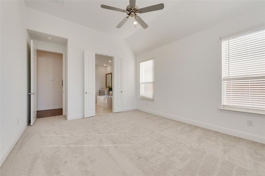 Unfurnished bedroom with ensuite bathroom, ceiling fan, lofted ceiling, and multiple windows