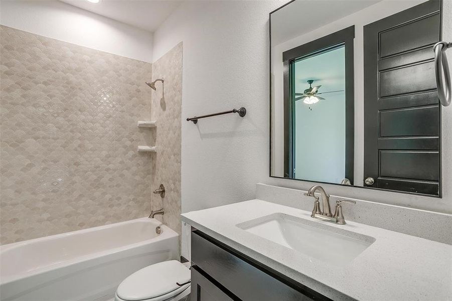 Full bathroom featuring ceiling fan, vanity, toilet, and tiled shower / bath combo