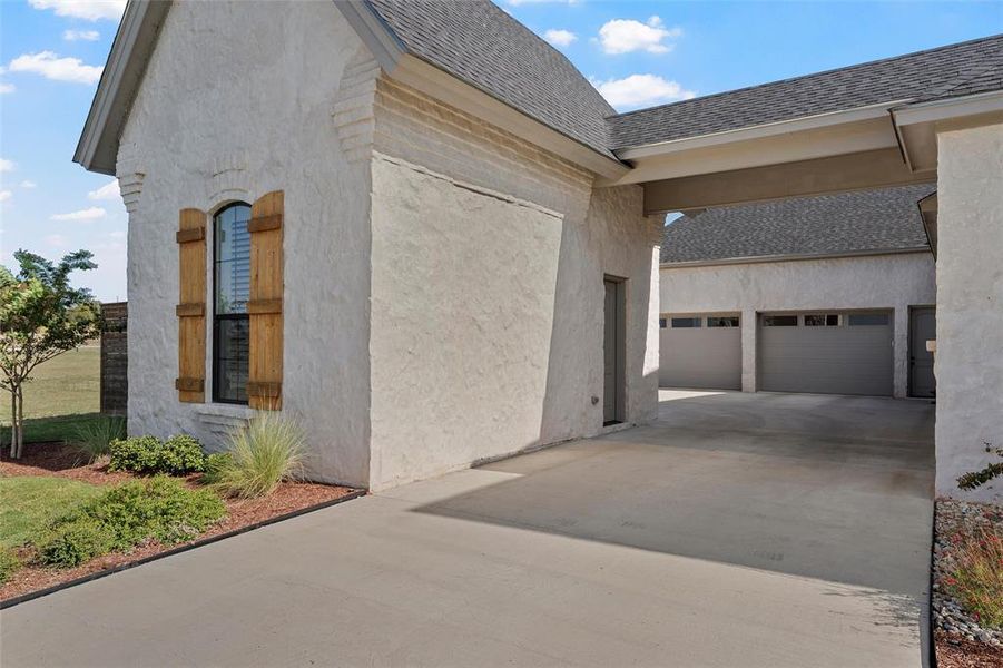 View of side of property with concrete driveway, a garage, roof with shingles, and stucco siding