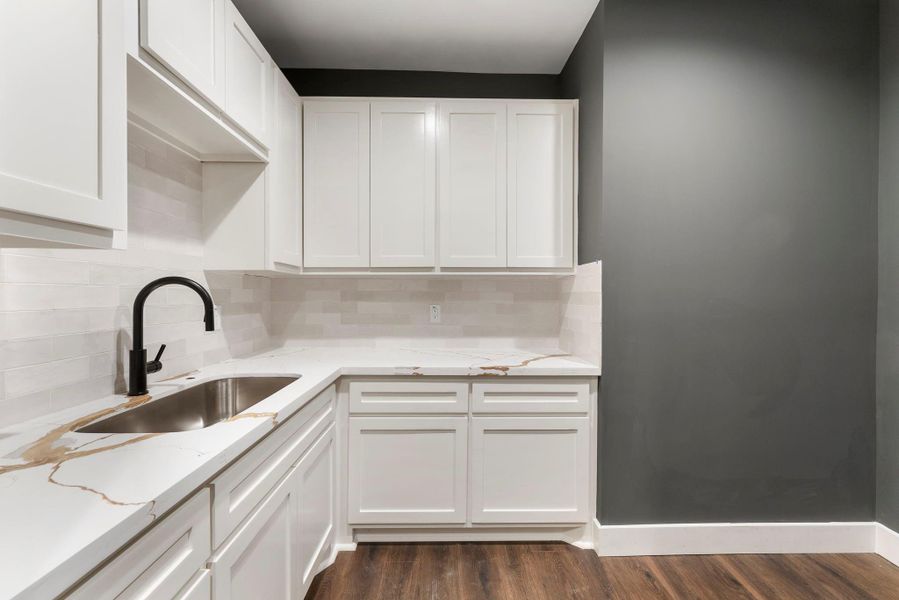 This dreamy laundry room features sleek white cabinetry with ample storage, over-sized sink, a modern black faucet, and elegant quartz countertops.