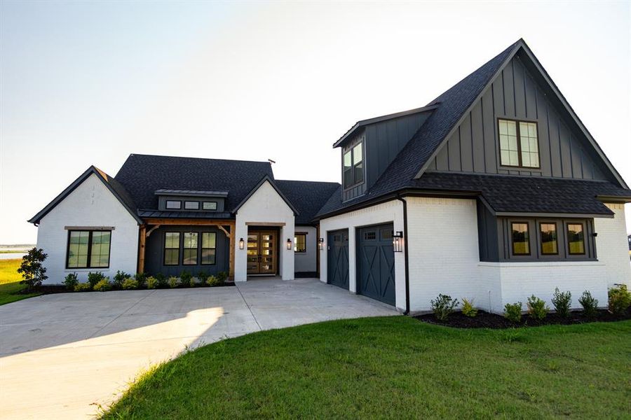Modern inspired farmhouse with a shingled roof, brick siding, concrete driveway, board and batten siding, and a front yard Modern inspired farmhouse with a shingled roof, brick siding, concrete driveway, board and batten siding, and a front yard