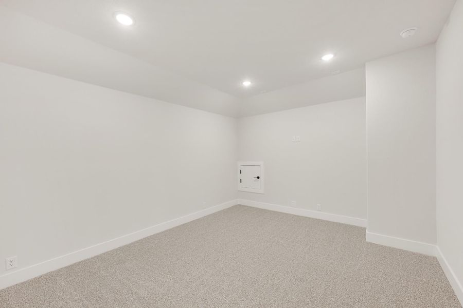 Empty basement room with white walls, gray carpet, recessed lighting, and small access door