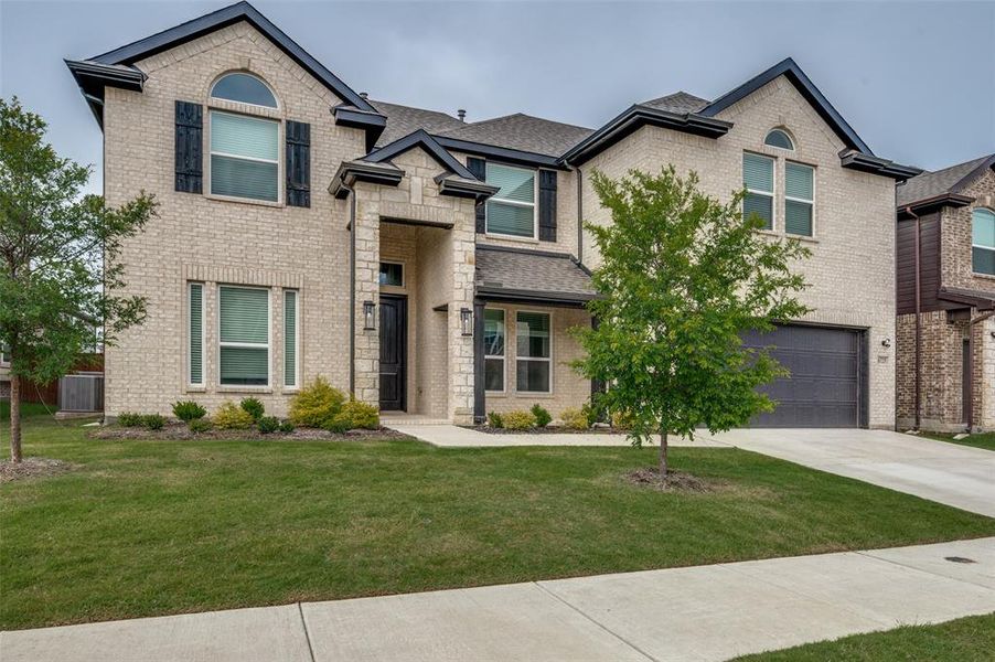 French country inspired facade with concrete driveway, brick siding, a front lawn, a garage, and roof with shingles French country inspired facade with concrete driveway, brick siding, a front lawn, a garage, and roof with shingles