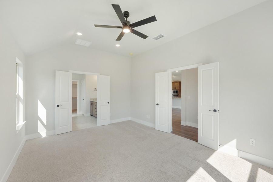 Empty bedroom with carpet, ceiling fan, and two open doors leading to bathroom and hallway Empty bedroom with carpet, ceiling fan, and two open doors leading to bathroom and hallway