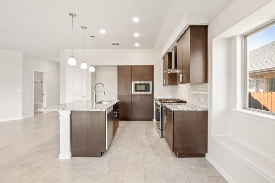 Kitchen with dark brown cabinets, granite island, stainless steel appliances, and pendant lights over tile floors Kitchen with dark brown cabinets, granite island, stainless steel appliances, and pendant lights over tile floors