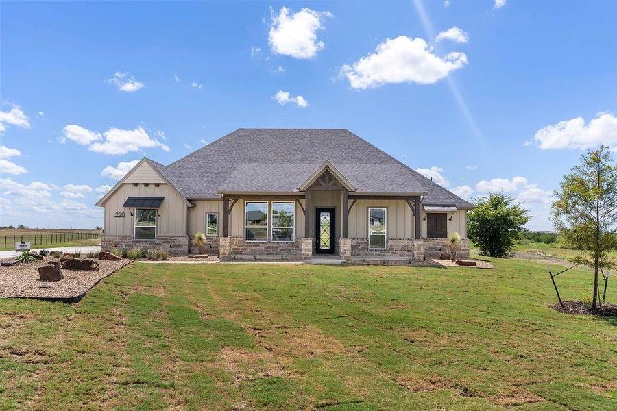 View of front of property with board and batten siding, stone siding, roof with shingles, and a front yard