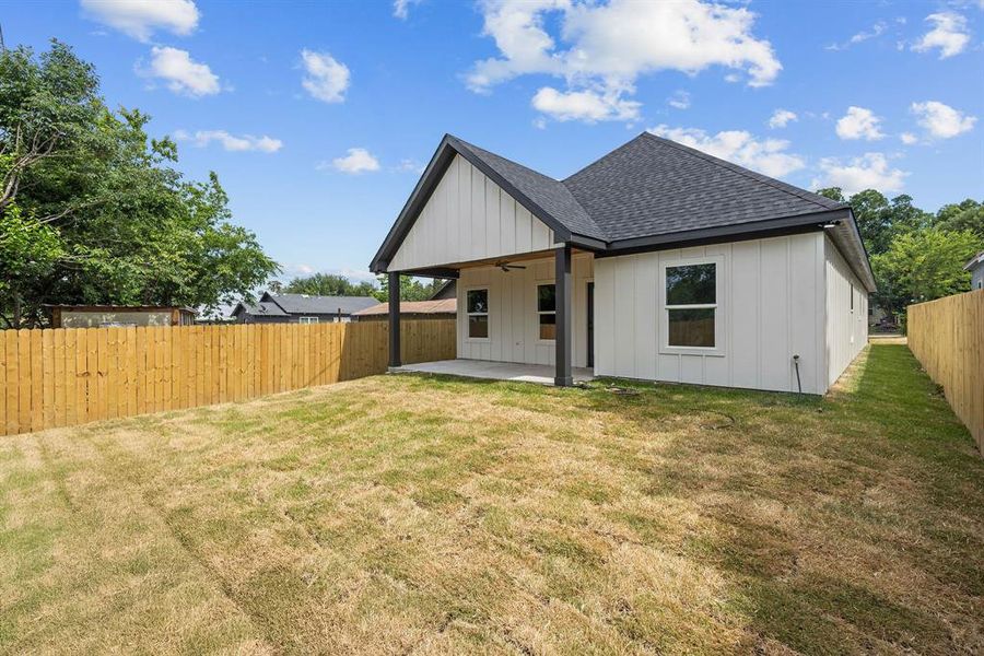 Spacious backyard featuring a full wood privacy fence, covered patio with a ceiling fan, and modern siding